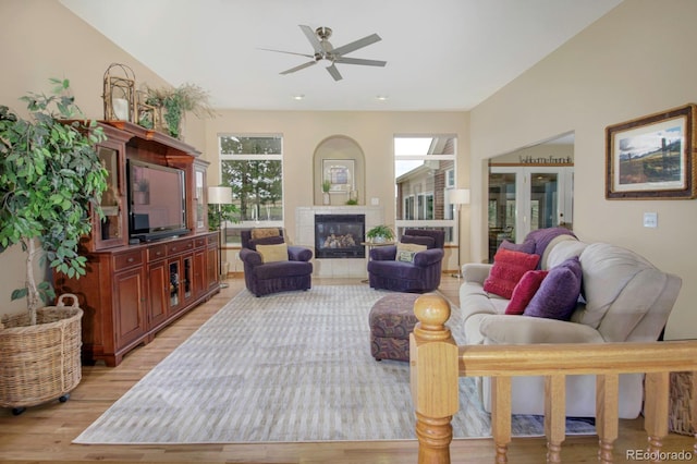 living room featuring a tile fireplace, light wood finished floors, and a ceiling fan