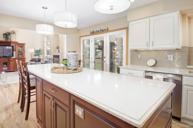 kitchen featuring stainless steel dishwasher, white cabinets, a center island, decorative light fixtures, and decorative backsplash