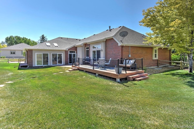 rear view of house featuring roof with shingles, a yard, brick siding, and fence