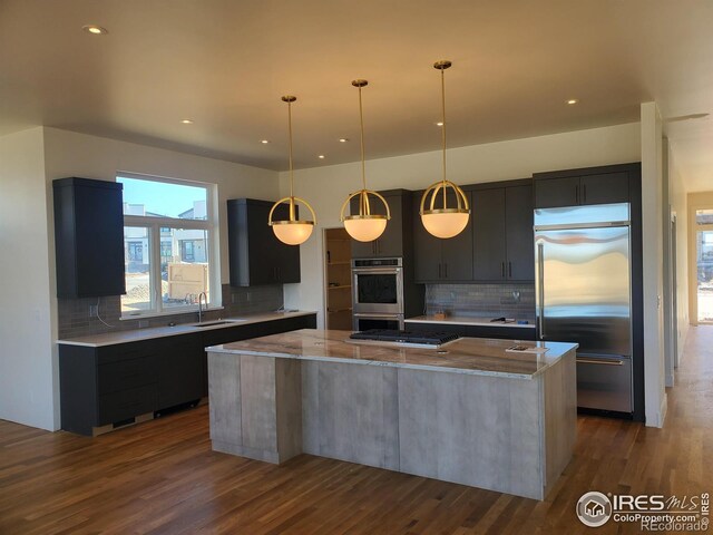 kitchen with a sink, a kitchen island, appliances with stainless steel finishes, light stone countertops, and dark wood finished floors