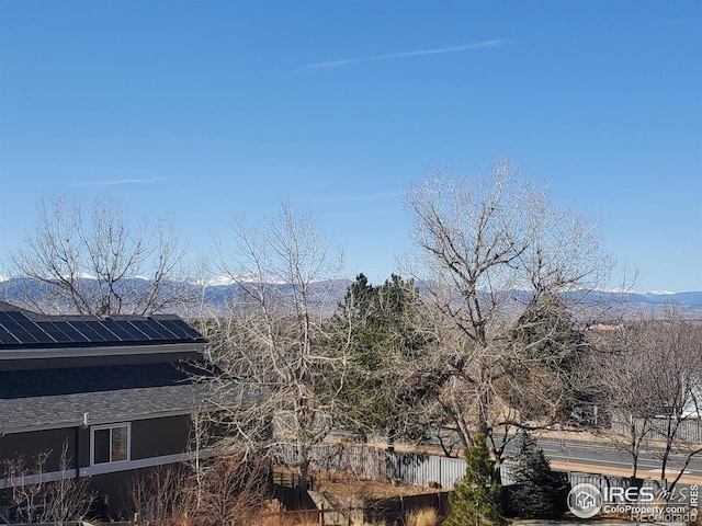 view of side of property featuring roof mounted solar panels, roof with shingles, a mountain view, and fence