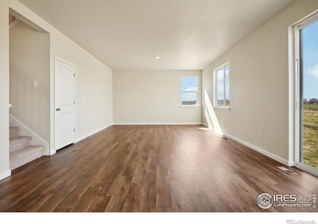 unfurnished room featuring visible vents, baseboards, dark wood-style flooring, and stairway