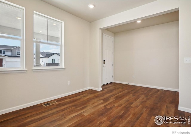 empty room featuring dark wood finished floors, recessed lighting, baseboards, and visible vents