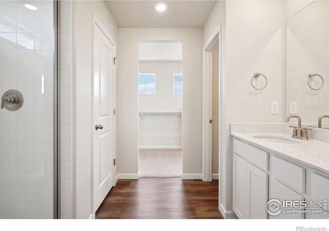 full bathroom featuring baseboards, tiled shower, wood finished floors, and vanity