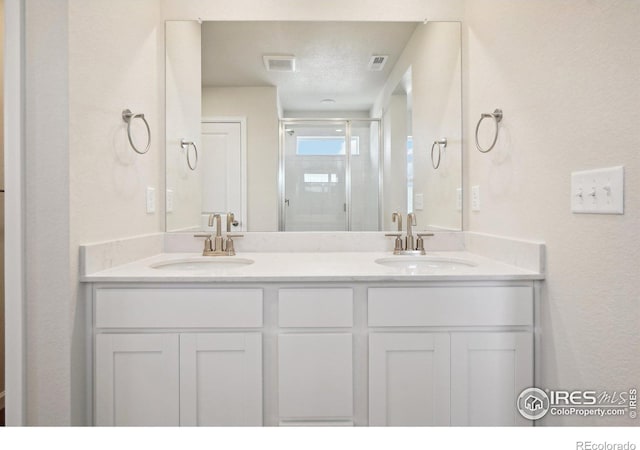 full bathroom featuring double vanity, visible vents, a stall shower, and a sink