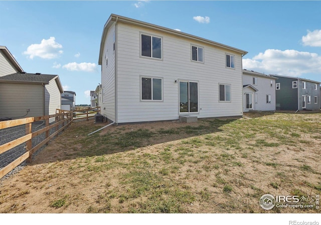 rear view of house featuring cooling unit, fence, and a yard