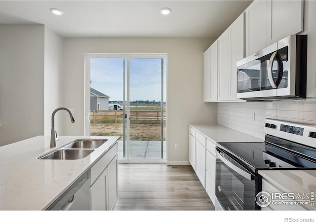 kitchen with decorative backsplash, white cabinets, light wood-style flooring, appliances with stainless steel finishes, and a sink