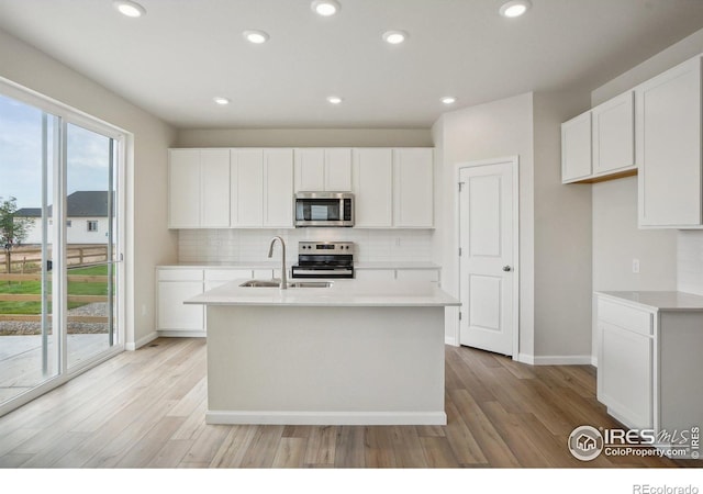 kitchen featuring an island with sink, stainless steel appliances, light countertops, white cabinetry, and a sink