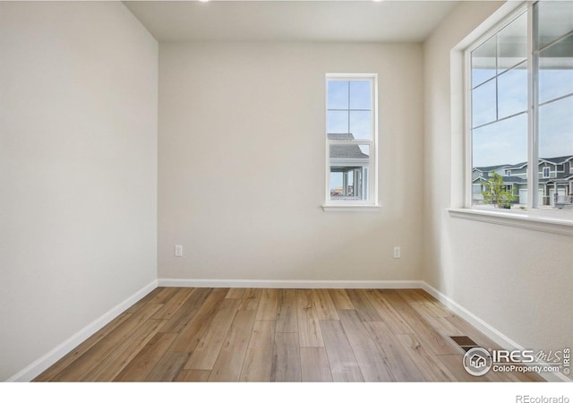 unfurnished room with light wood-type flooring, visible vents, and baseboards