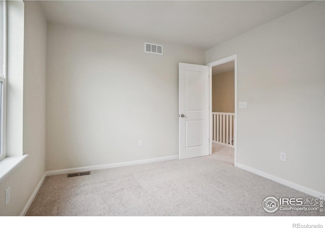 empty room featuring light carpet, baseboards, and visible vents