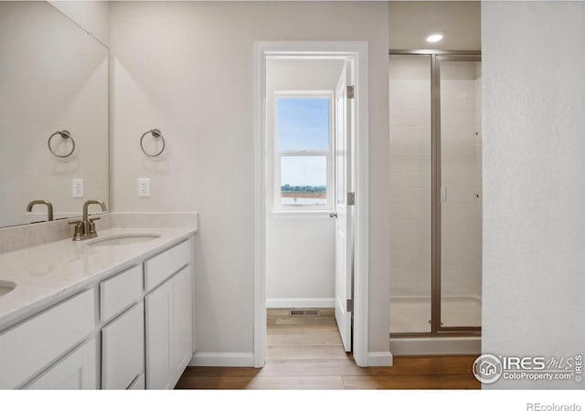 full bathroom with double vanity, a sink, a shower stall, wood finished floors, and baseboards