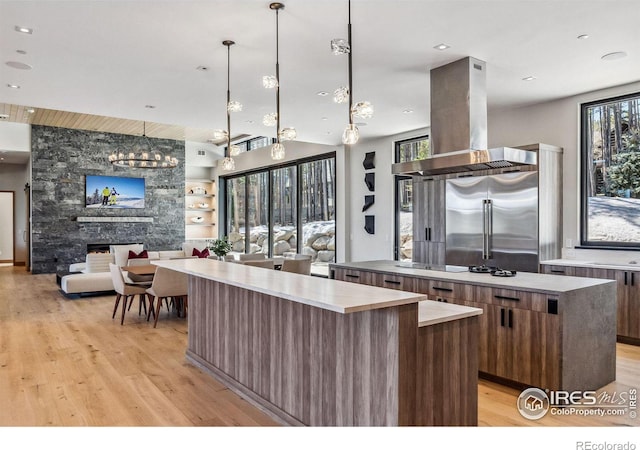 kitchen featuring a stone fireplace, decorative light fixtures, light hardwood / wood-style flooring, island exhaust hood, and a large island