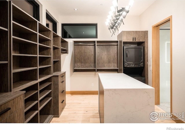 spacious closet with stacked washer and clothes dryer, light hardwood / wood-style floors, and a notable chandelier