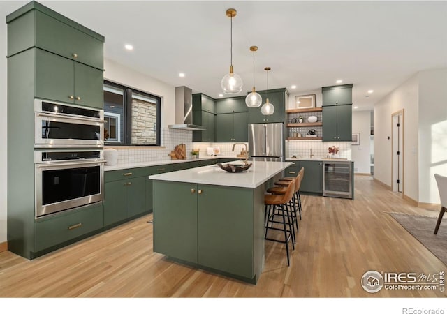 kitchen featuring appliances with stainless steel finishes, beverage cooler, wall chimney exhaust hood, decorative light fixtures, and a center island