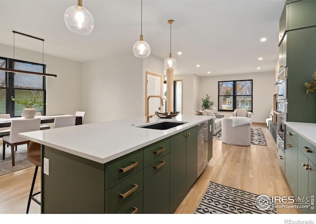 kitchen featuring a kitchen island with sink, sink, a kitchen breakfast bar, hanging light fixtures, and light hardwood / wood-style flooring