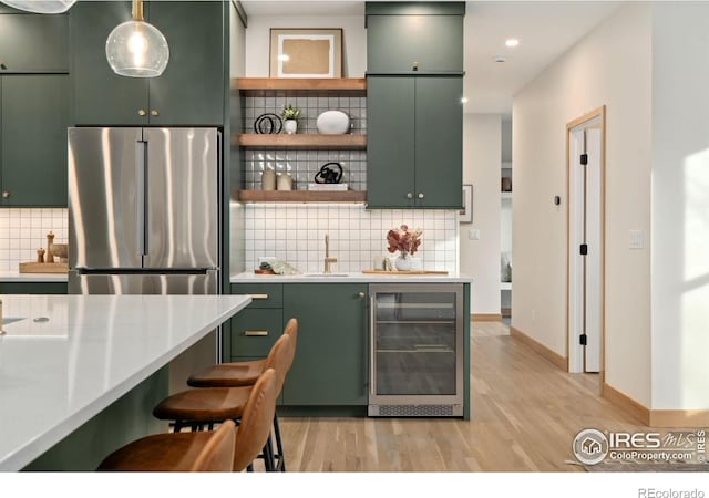 kitchen with beverage cooler, hanging light fixtures, backsplash, and stainless steel fridge