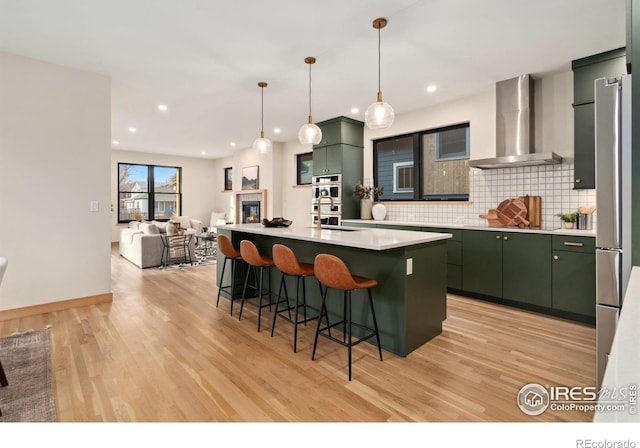 kitchen featuring backsplash, light wood-type flooring, wall chimney exhaust hood, and green cabinets