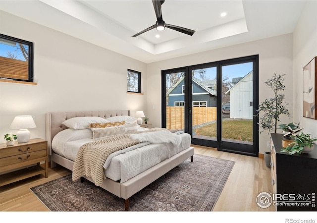 bedroom featuring a raised ceiling, access to exterior, ceiling fan, and light hardwood / wood-style flooring