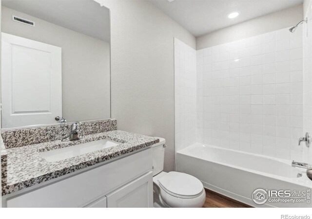 full bathroom with tiled shower / bath combo, hardwood / wood-style flooring, toilet, and vanity with extensive cabinet space