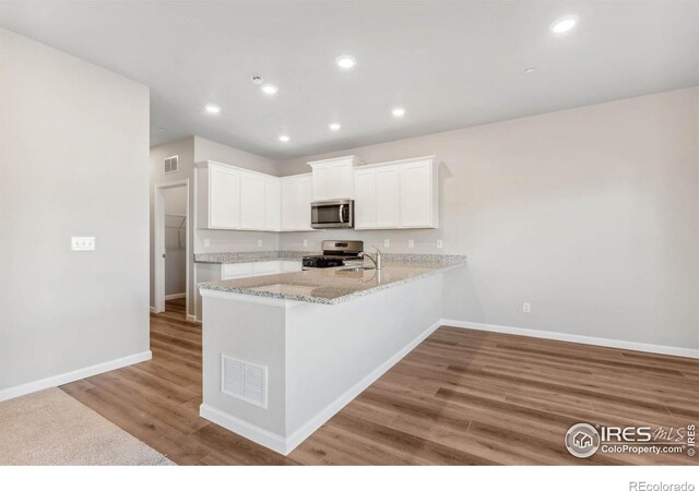 kitchen with kitchen peninsula, stainless steel appliances, hardwood / wood-style flooring, light stone countertops, and white cabinetry