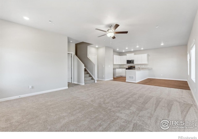 unfurnished living room featuring light carpet, sink, and ceiling fan