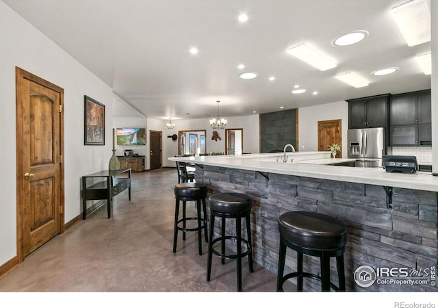 kitchen with a kitchen bar, decorative backsplash, stainless steel fridge, and an inviting chandelier