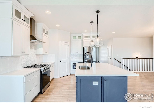 kitchen featuring appliances with stainless steel finishes, a center island with sink, wall chimney range hood, and white cabinetry