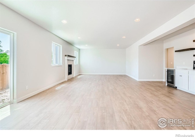 unfurnished living room featuring a wealth of natural light, beverage cooler, and light wood-type flooring