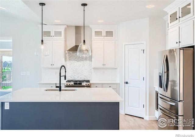 kitchen with appliances with stainless steel finishes, light hardwood / wood-style flooring, wall chimney exhaust hood, and decorative light fixtures