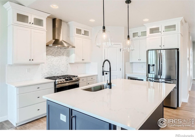 kitchen with appliances with stainless steel finishes, sink, wall chimney range hood, and an island with sink