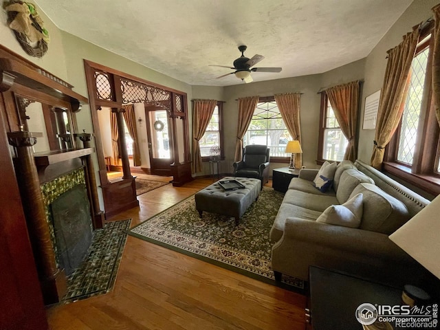 living room with ceiling fan, wood-type flooring, a tiled fireplace, and a textured ceiling