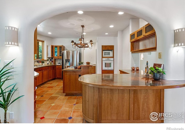 kitchen with an inviting chandelier, kitchen peninsula, decorative light fixtures, white appliances, and light tile patterned floors