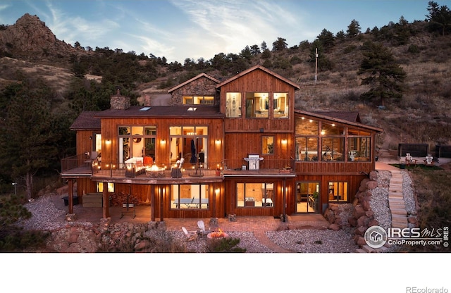 back house at dusk with a mountain view, a patio area, and a balcony