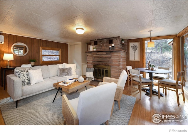 living room with a wall mounted air conditioner, wood-type flooring, a stone fireplace, and wooden walls