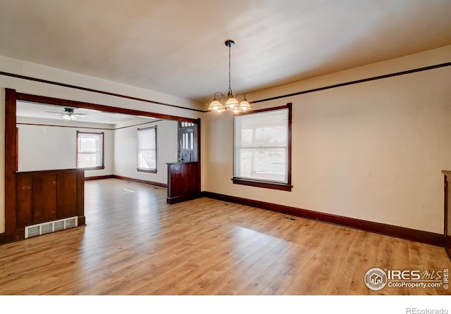 unfurnished room with ceiling fan with notable chandelier and hardwood / wood-style flooring