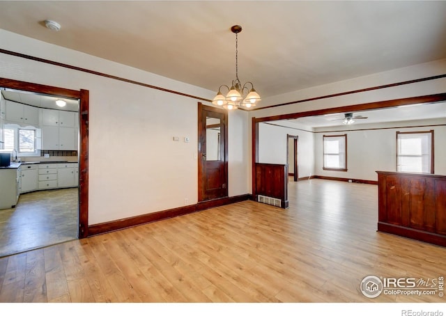 spare room with ceiling fan with notable chandelier, sink, a healthy amount of sunlight, and light hardwood / wood-style floors