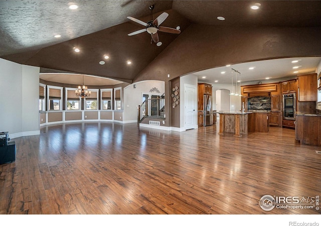 unfurnished living room with a textured ceiling, high vaulted ceiling, ceiling fan with notable chandelier, and dark hardwood / wood-style flooring