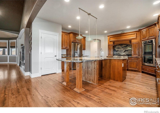 kitchen featuring a spacious island, light stone countertops, appliances with stainless steel finishes, and light hardwood / wood-style floors