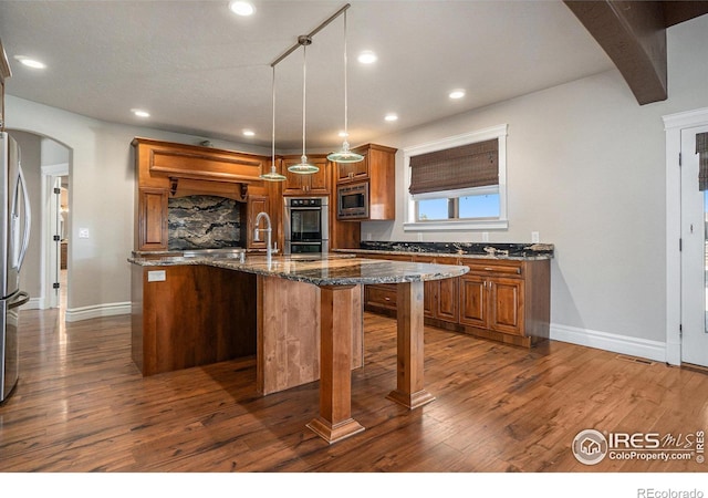 kitchen featuring a kitchen island with sink, dark stone countertops, dark wood-type flooring, pendant lighting, and stainless steel appliances