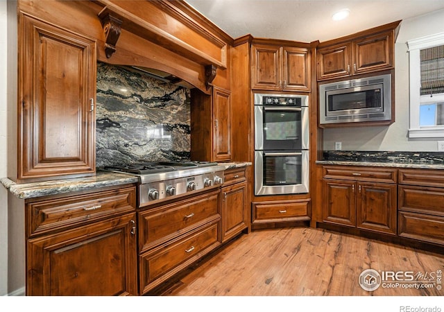 kitchen with appliances with stainless steel finishes, dark stone counters, light wood-type flooring, and decorative backsplash