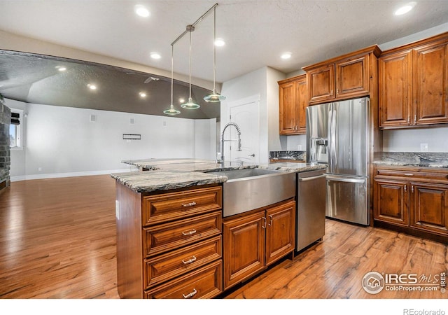 kitchen featuring light hardwood / wood-style floors, a kitchen island with sink, stainless steel appliances, and pendant lighting