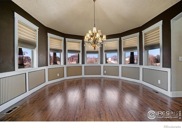 unfurnished dining area with a chandelier, hardwood / wood-style flooring, and a textured ceiling