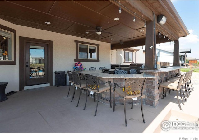 view of patio featuring ceiling fan, grilling area, and a bar