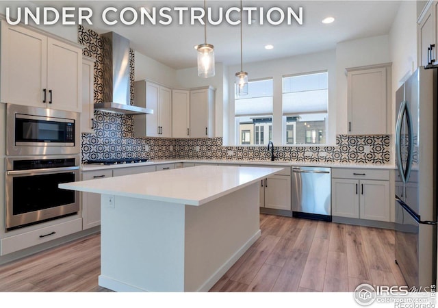 kitchen with a center island, stainless steel appliances, wall chimney range hood, and light hardwood / wood-style floors