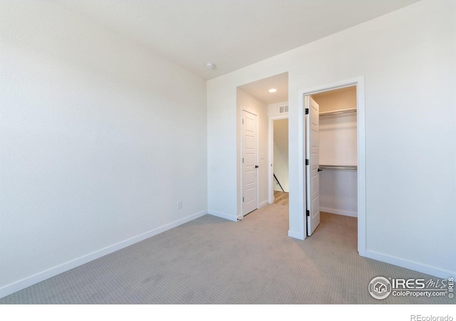 unfurnished bedroom with a walk in closet, light carpet, and a closet