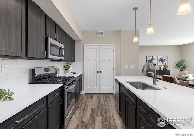 kitchen with tasteful backsplash, stainless steel appliances, decorative light fixtures, hardwood / wood-style floors, and sink