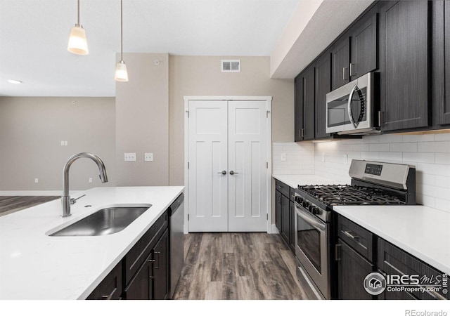 kitchen with hardwood / wood-style floors, sink, appliances with stainless steel finishes, tasteful backsplash, and pendant lighting