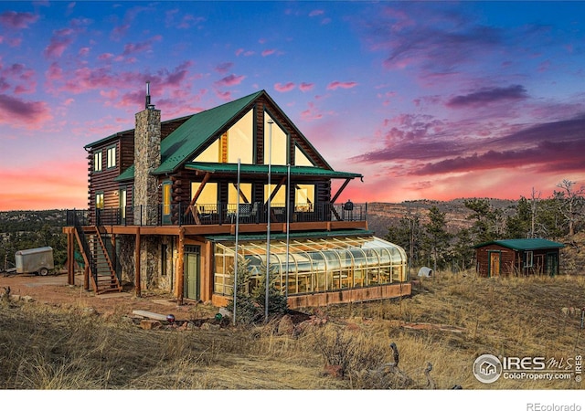 back house at dusk featuring an outdoor structure, a deck, and a sunroom