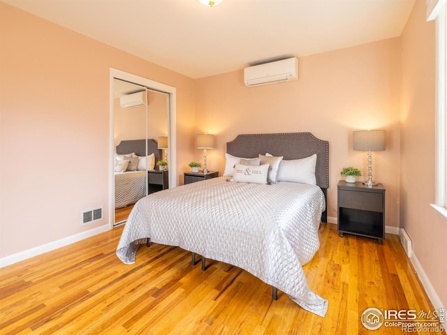 bedroom with a closet, a wall mounted air conditioner, and light wood-type flooring