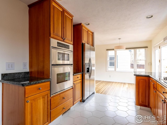 kitchen featuring hanging light fixtures, dark stone countertops, light hardwood / wood-style floors, a textured ceiling, and appliances with stainless steel finishes